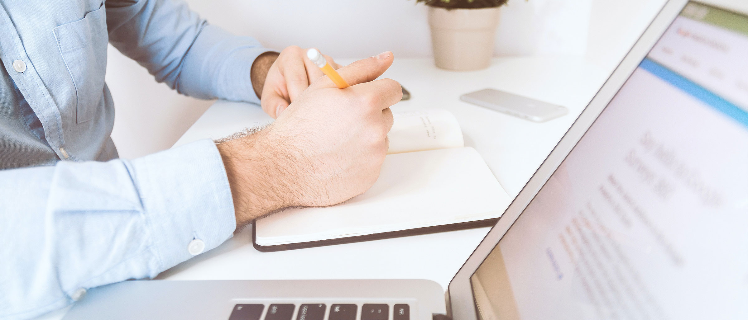 Person writing in notebook beside laptop