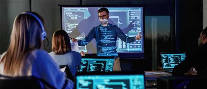 Man presenting to group of coders in front of projection screen