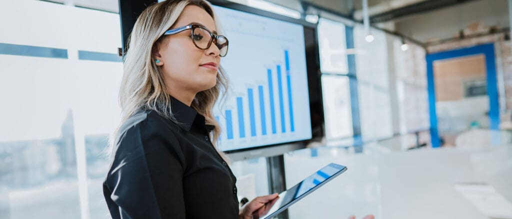 A business woman holding a tablet in front of a large screen