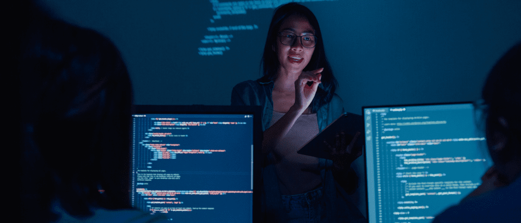 Two screens with code and woman holding tablet