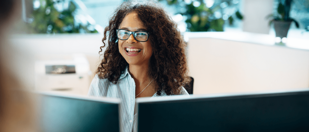 Woman smiling in front of two computer screens