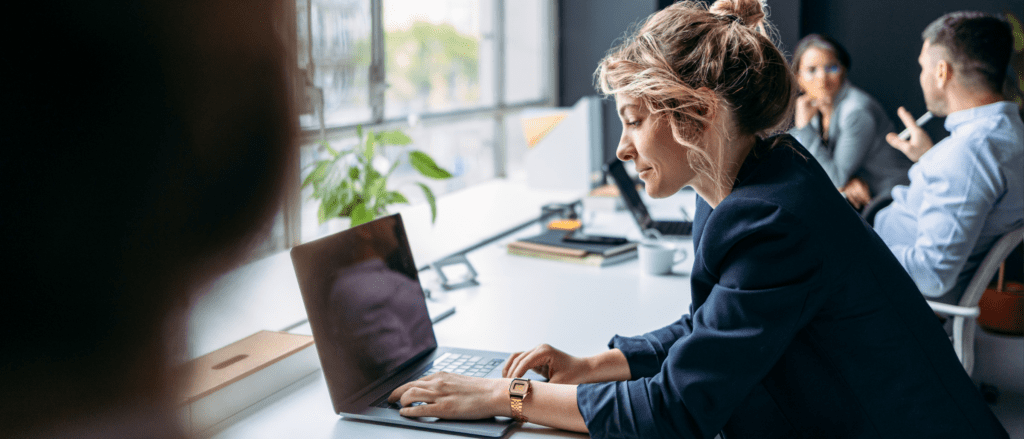 Woman working on laptop with other professionals in the background