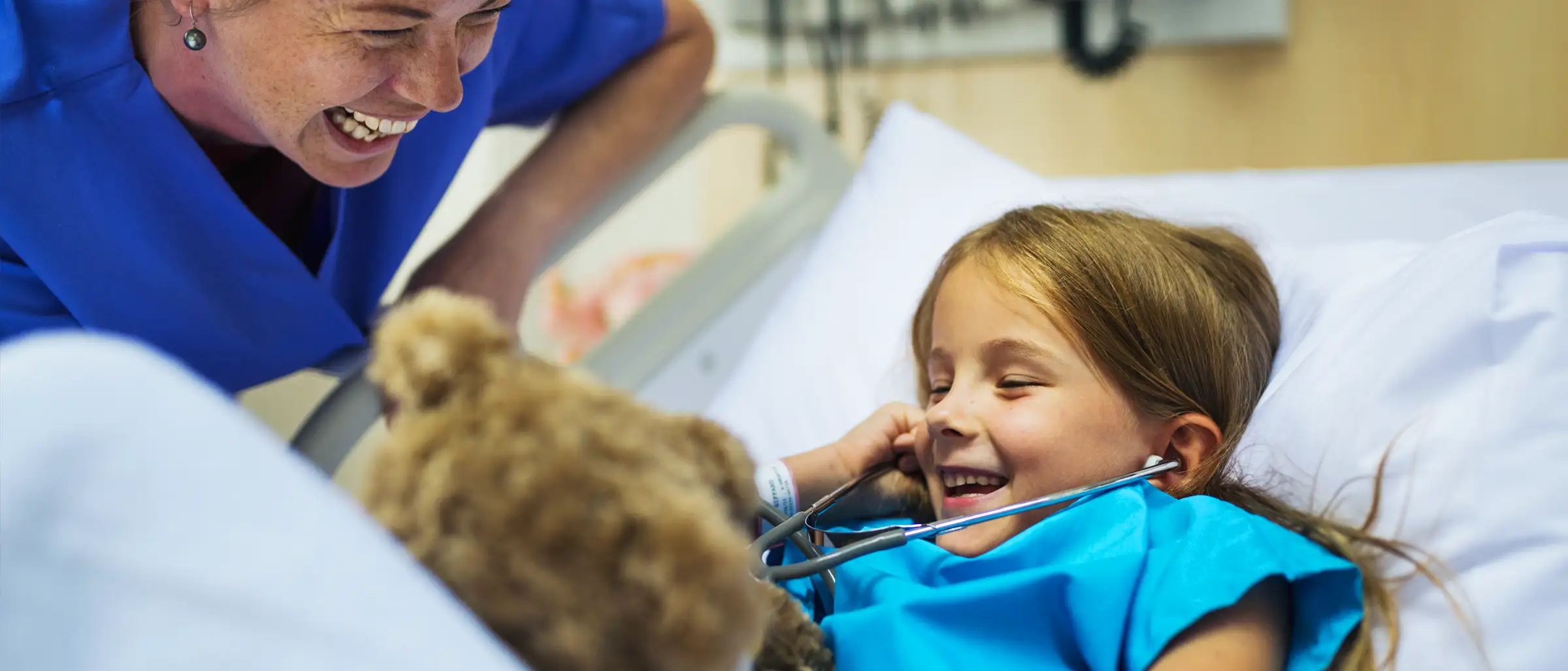 Child and medical professional use stethoscope on teddy bear