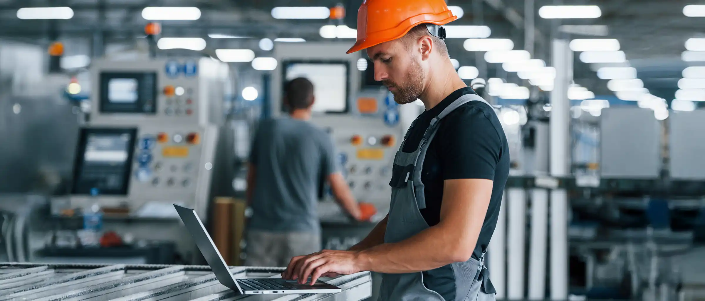 Man with hardhat working on laptop in manufacturing plant