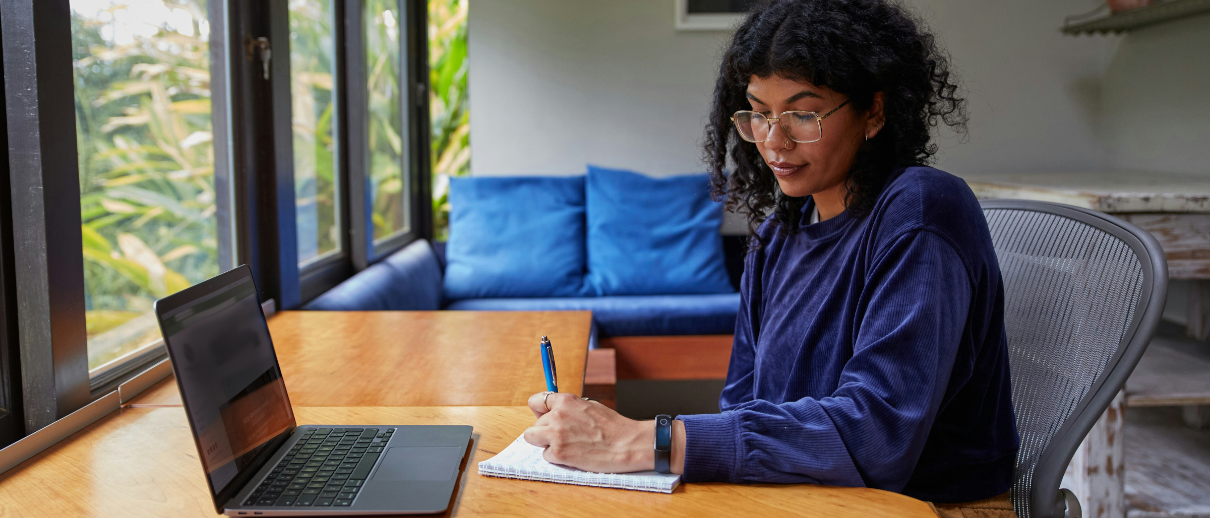 Woman sitting at a home office setup writing on paper