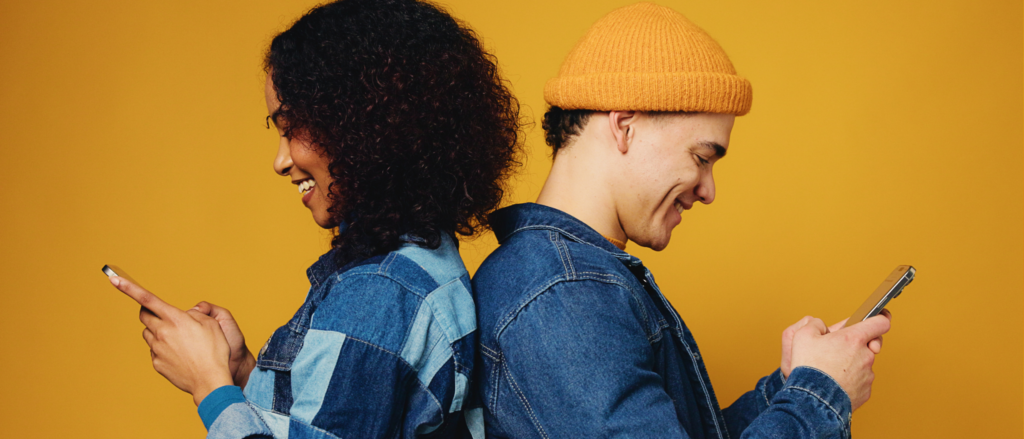 Two people back to back looking at their phones and smiling