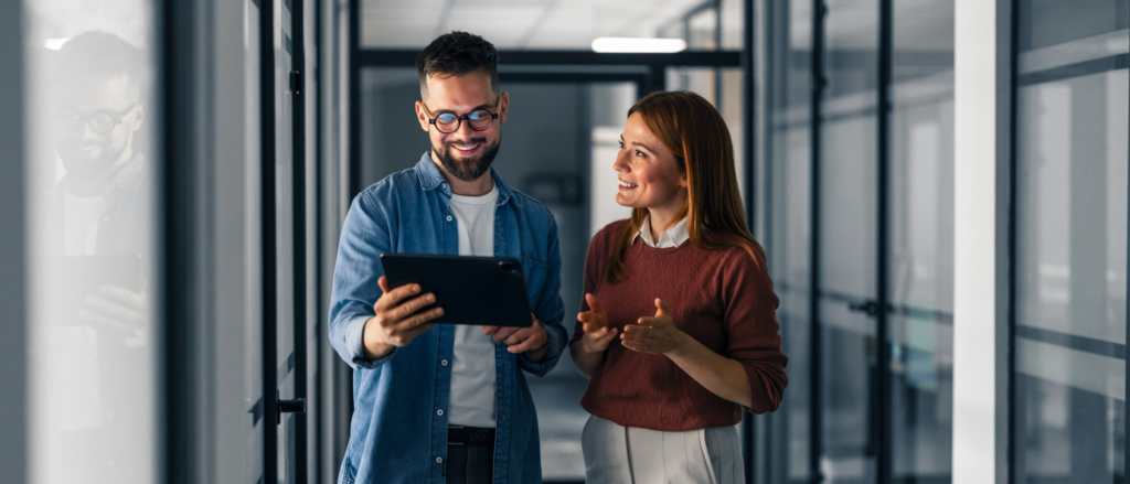 Two professionals looking at a tablet in a corporate hallway