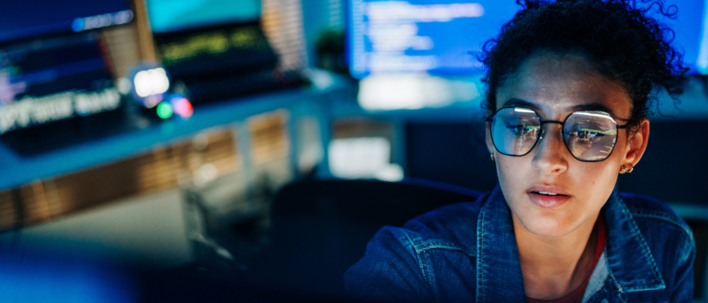 Developer sitting in dark workspace surrounded by screens with computer code on them