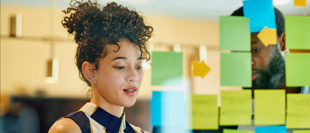 Two colleagues talking while arranging sticky notes on the other side of a transparent board