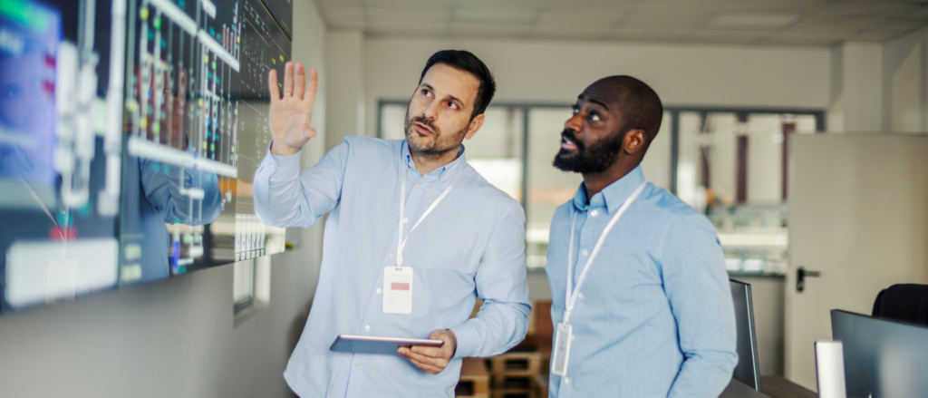 Two engineers reviewing schematics on a large monitor