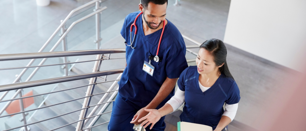 Two medical professionals in blue scrubs walking up a staircase in a medical facility