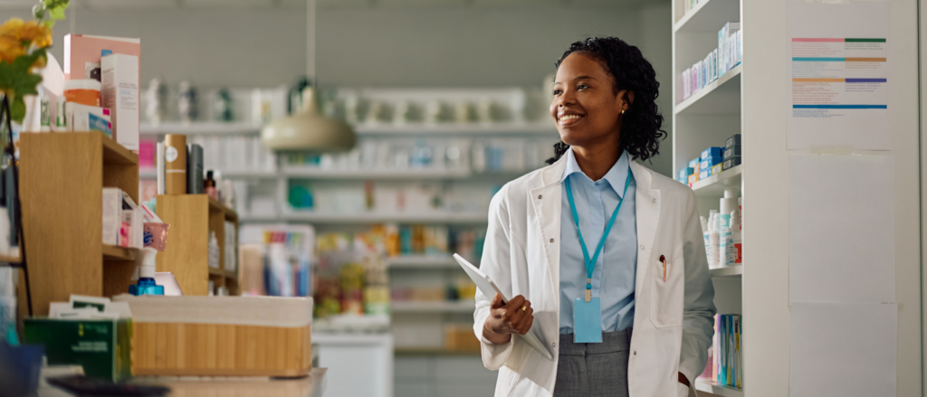 Pharmacist in white coat walking past shelves of medications