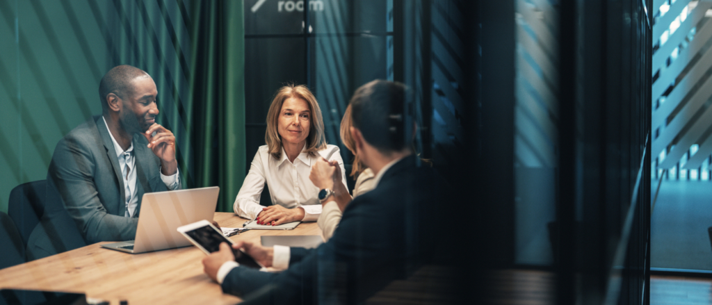 Colleagues in discussion around a conference table in a modern meeting room.